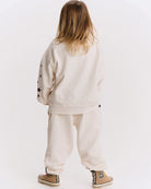 A child viewed from behind wearing a cream-colored sweatshirt and jogger pants set, with black embroidered stars on the sleeve and tan sneakers.