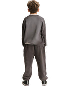 A child viewed from the back wearing a dark gray sweatshirt and matching sweatpants, with black sneakers, against a plain white background.
