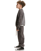 A child model shown in profile wearing a dark gray crewneck sweatshirt with black star embroidery on the sleeve, matching dark gray sweatpants, and black low-top sneakers, against a plain white background.