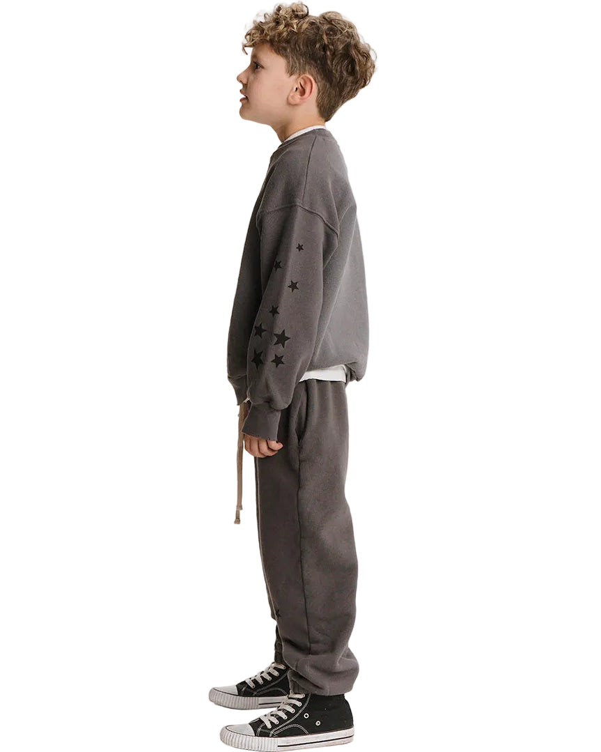 A child model shown in profile wearing a dark gray crewneck sweatshirt with black star embroidery on the sleeve, matching dark gray sweatpants, and black low-top sneakers, against a plain white background.